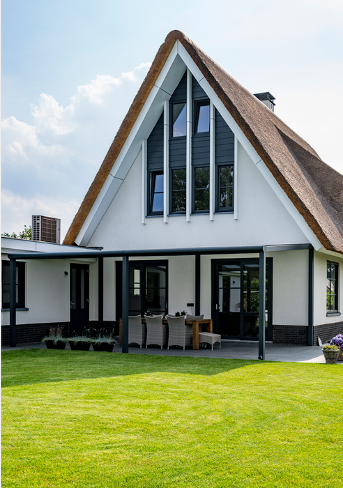 Photo of a large white house with a triangular tall roof and it has a Lean-To pergola on the back of it, over its patio doors