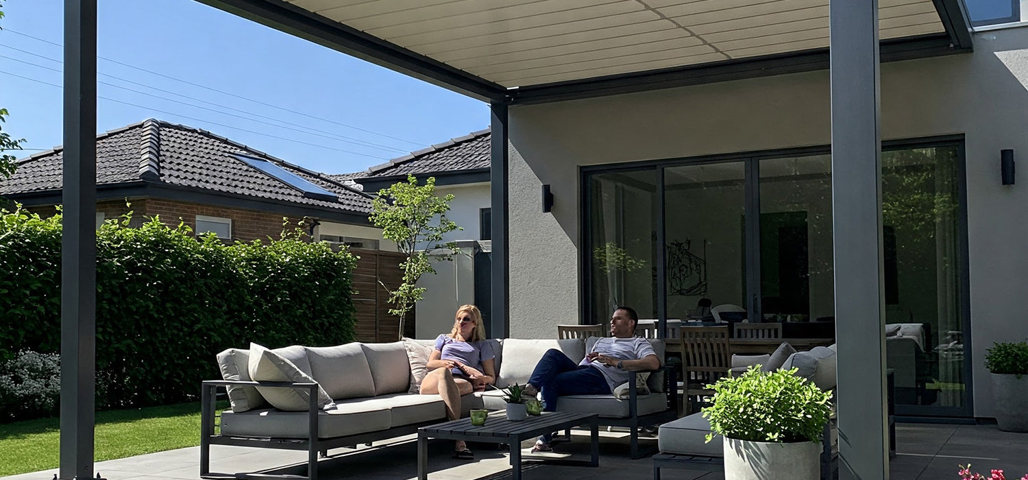 A retractable pergola with two people sitting underneath it on a patio