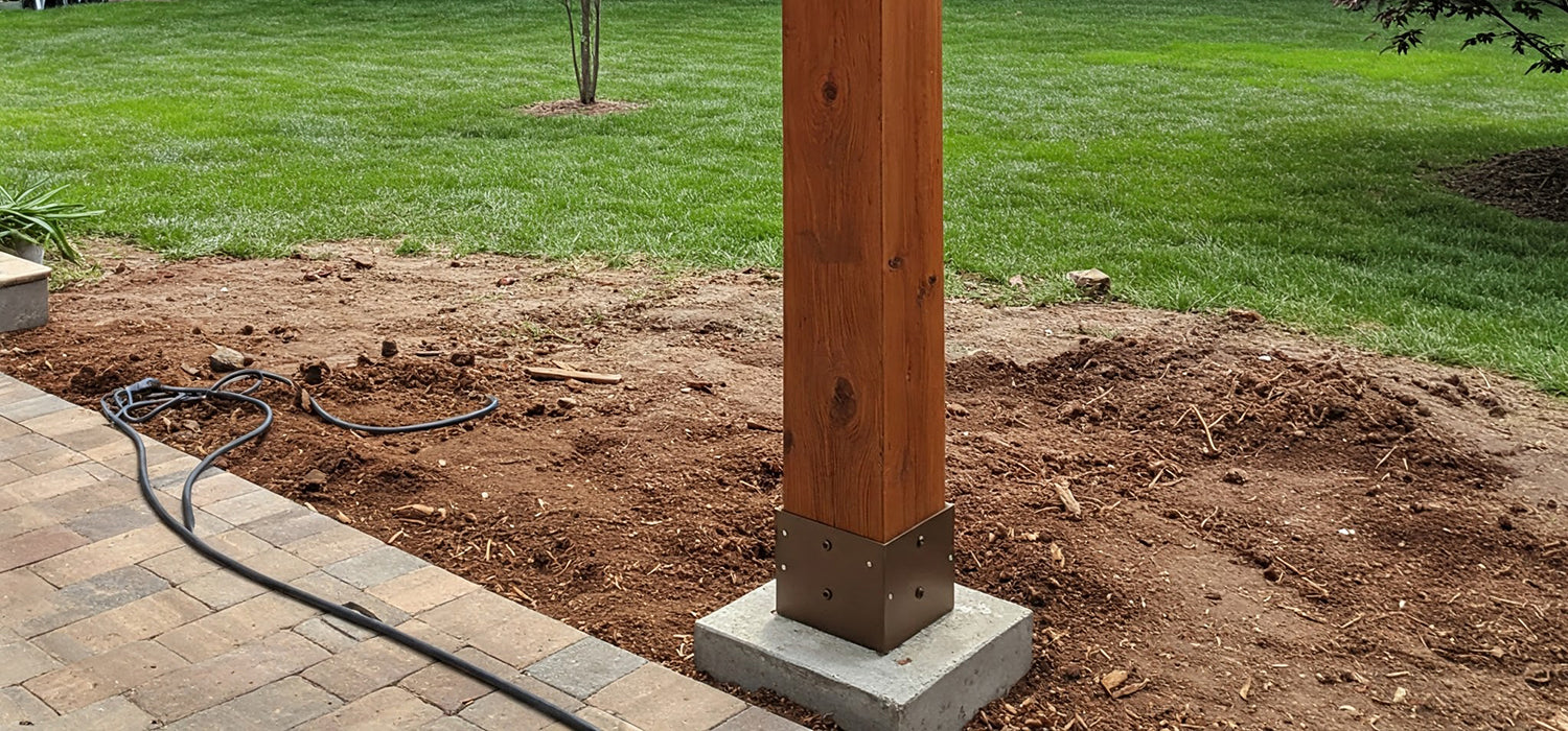 A wooden pergola post installed on a concrete base in a backyard.