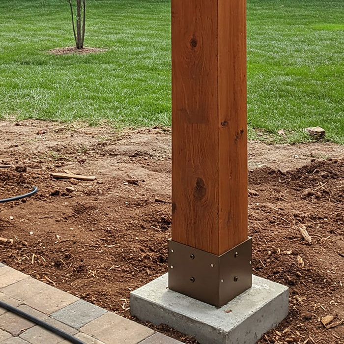 A wooden pergola post installed on a concrete base in a backyard.