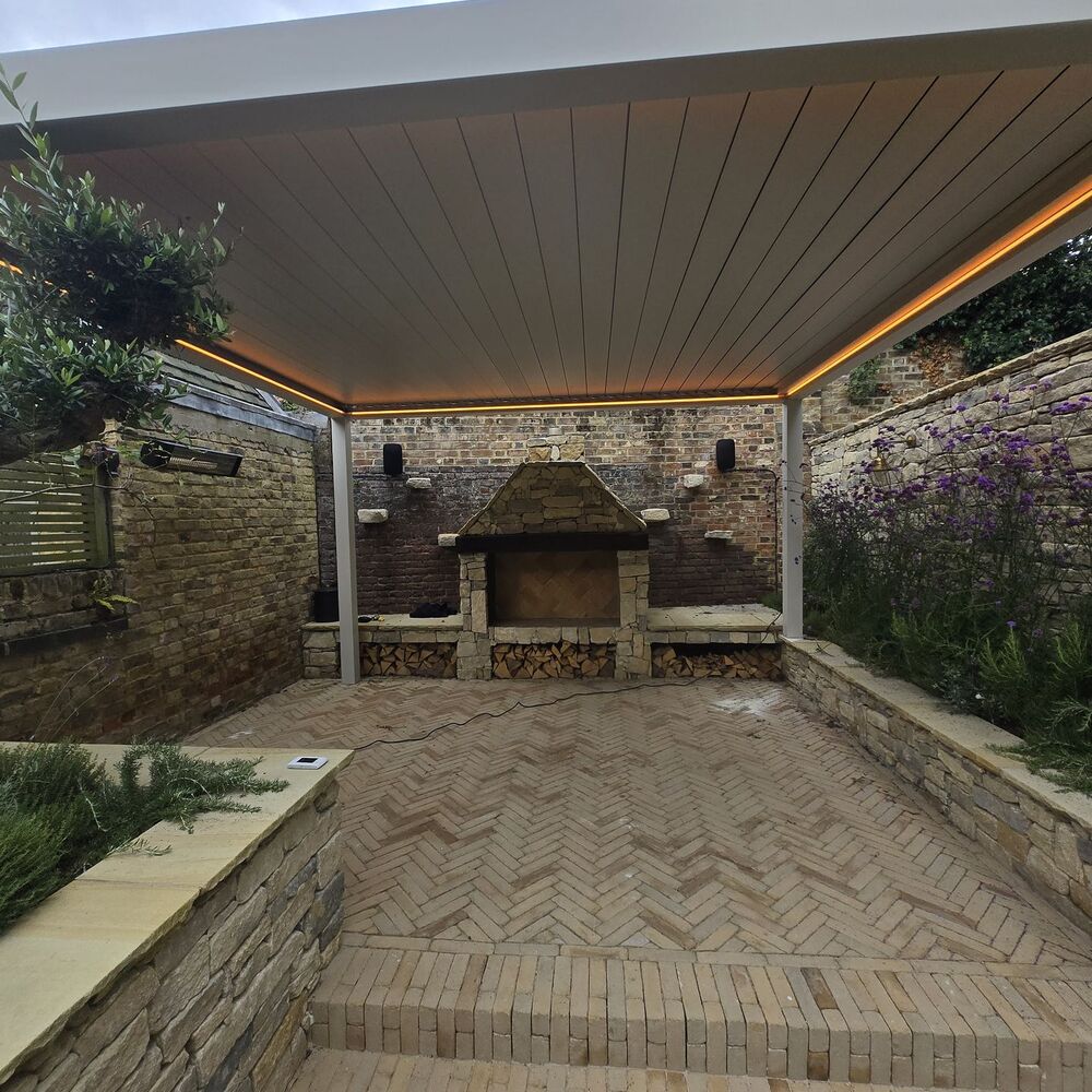 Outdoor patio with brick flooring, stone wall, and a pergola covered barbecue area.