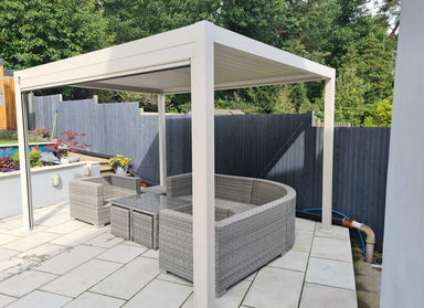 Patio with outdoor furniture under a white pergola, surrounded by greenery.